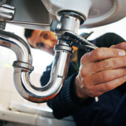 Expert plumber in BC using a wrench to repair bathroom sink pipes, focusing on hands and plumbing details for HVAC services.