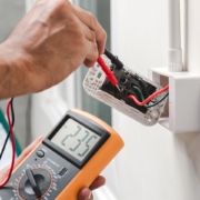 An HVAC technician in BC checks outlet voltage with a digital multimeter, showing 235 volts for safe electrical service.