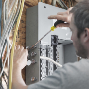Technician repairs wiring in electrical panels, surrounded by cables on a wooden wall—expert HVAC service in British Columbia.