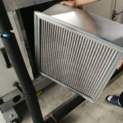 A person in socks changes a large metal-framed air filter in an industrial HVAC unit, common for BC HVAC maintenance services.