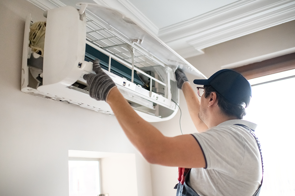 HVAC technician in gloves services a wall-mounted AC unit in a bright BC home, highlighting expert cooling system solutions.