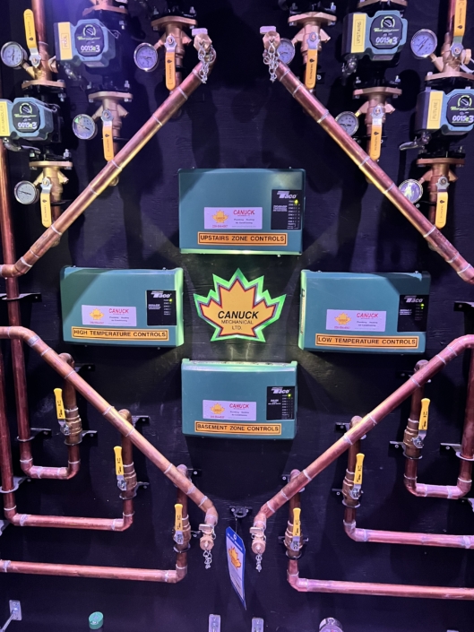 Copper pipes and green “Canuck” control boxes for zoned HVAC in BC, with gauges and valves neatly arranged on the wall.