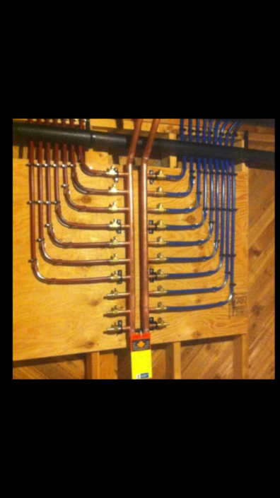 Plumbing manifold with labeled copper and blue PEX pipes, expertly installed on wood in a BC building under construction.