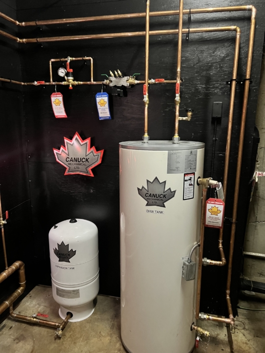 Modern water heating system with DHWTANK, expansion tank, copper pipes, gauges, and Canuck maple leaf signs in BC HVAC install.