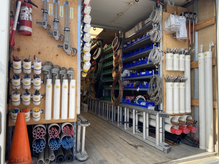 A tidy HVAC service truck in BC, with labeled bins holding pipes, hoses, fittings, and tools; orange safety cone on the floor.