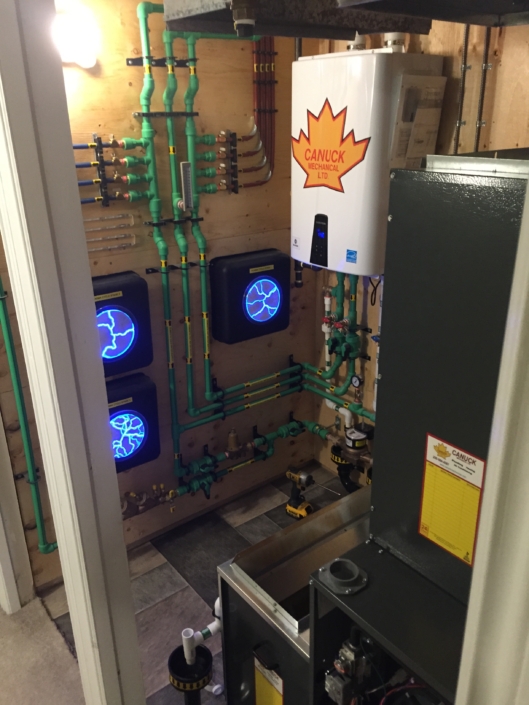 Modern mechanical room in BC featuring a CANUCK heating system, organized pipes, gauges, and blue-lit HVAC control panels.