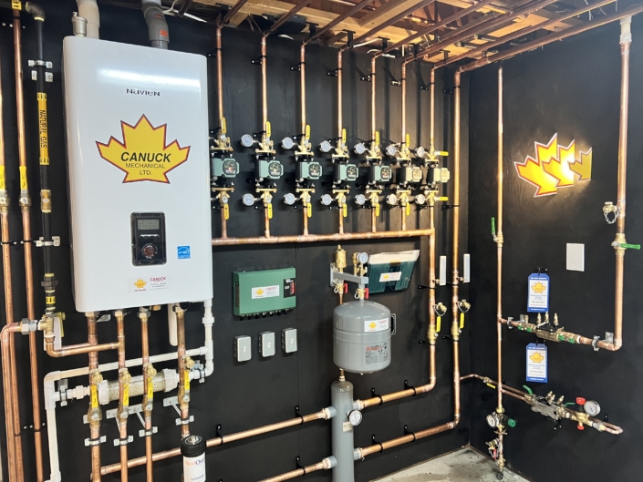 A BC mechanical room with copper piping, valves, tankless water heater, gauges, expansion tank, and Canuck Mechanical LTD logos.